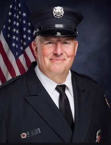 A Healing The Hero participant in firefighter dress uniform in front of an American flag